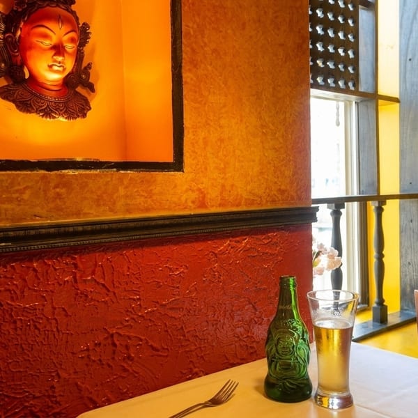Restaurant interior with a Buddha statue on the wall, a drink, and a fork on a white tablecloth.