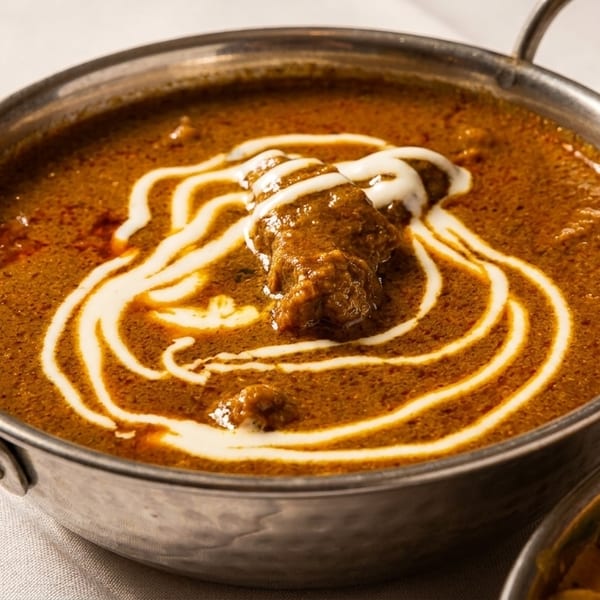 Rich brown curry with a swirl of cream and a piece of meat in a metal bowl.