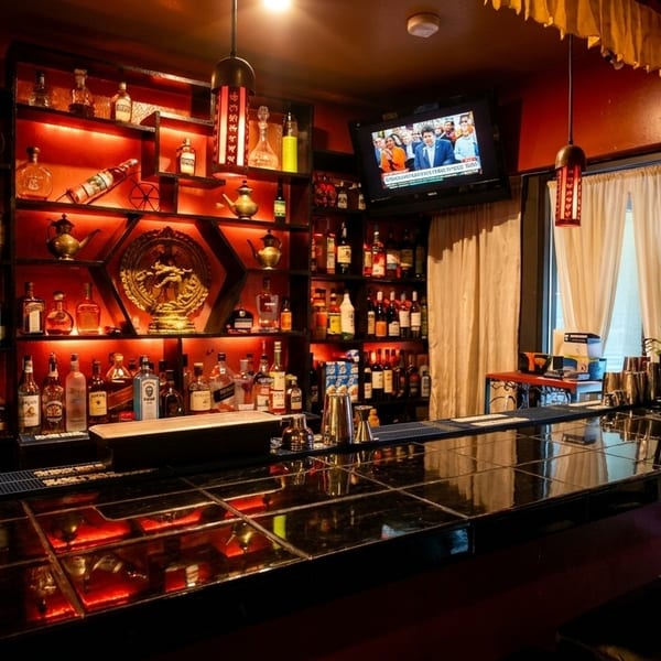 A dimly lit bar with shelves of liquor bottles, a TV, and a dark tiled counter.