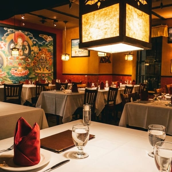 A restaurant dining room with white-clothed tables, red napkins, and a large colorful mural on the wall.