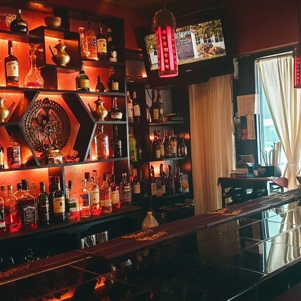 A dimly lit bar with shelves of liquor bottles, decorative items, and a TV screen.