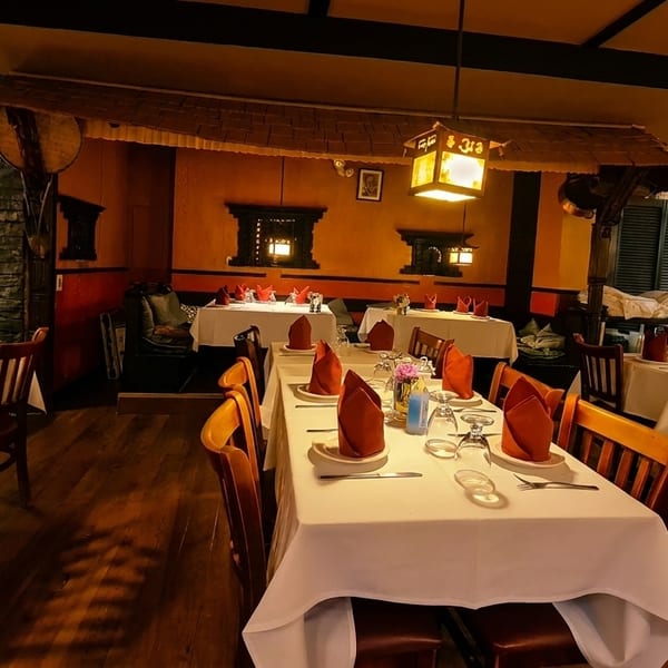 Warmly lit restaurant interior with set tables, dark wood chairs, and stone accent walls.