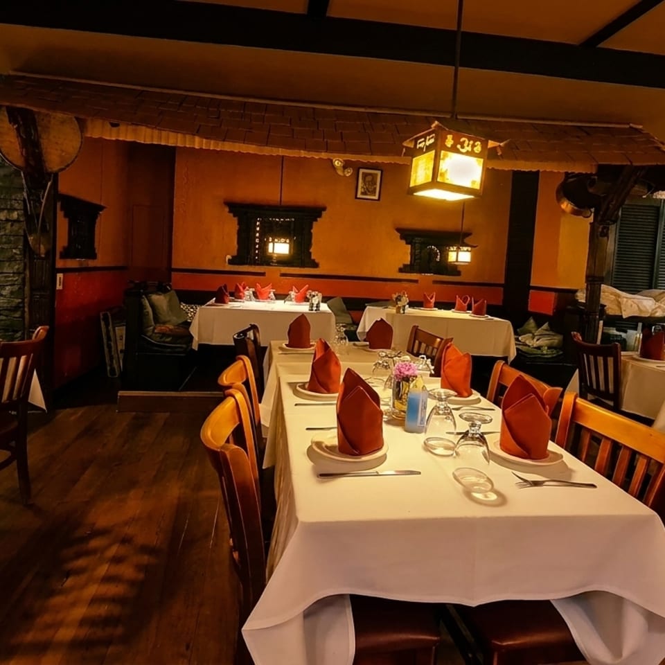 Warmly lit restaurant interior with set tables, dark wood chairs, and stone accent walls.