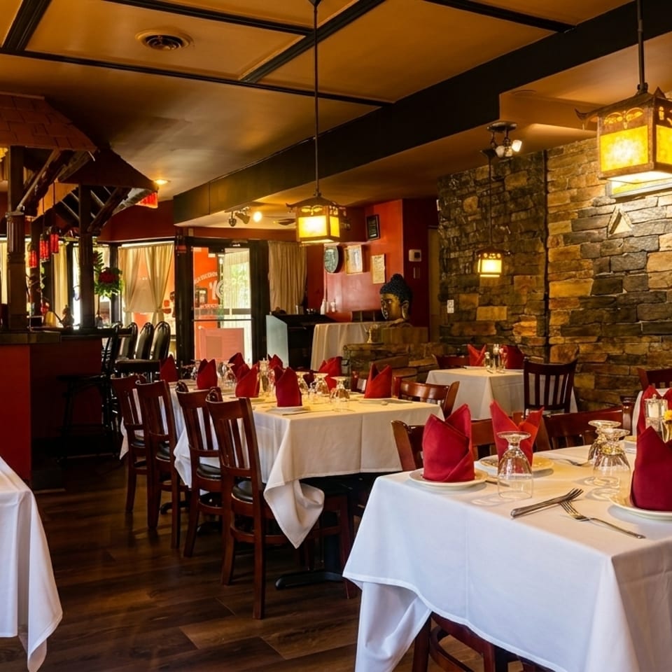 Restaurant dining room with white tablecloths, red napkins, dark wood chairs, and stone walls.