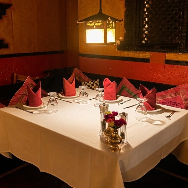 Cozy restaurant corner with a set table, red napkins, decorative pillows, and warm lighting.