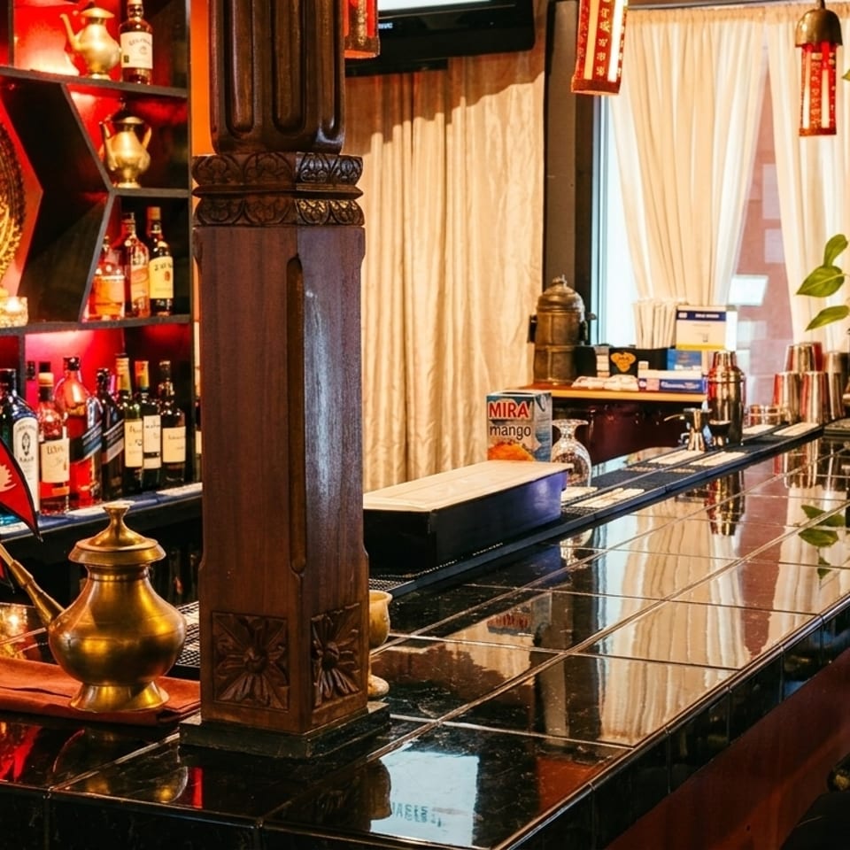 Restaurant bar with red-lit shelves of liquor bottles, decorative teapots, and a Nepalese flag.