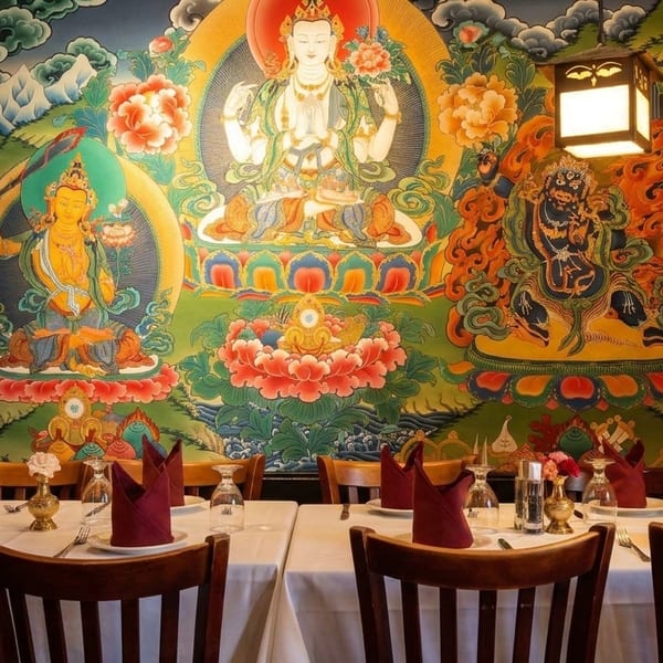 Restaurant dining room with tables set against a vibrant, colorful mural depicting Buddhist deities.